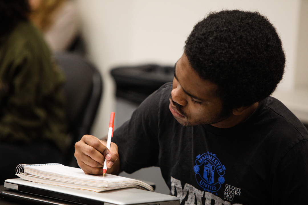 A male student leaning over his desk and taking notes during a lecture