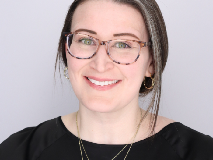 A headshot photo of Dr. Lauren King. She is wearing a black shirt, two gold necklaces, large tortoise shell glasses, and has her hair back behind her head.